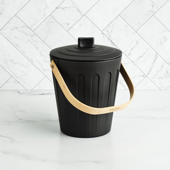Black trash bin with a beige handle on a white marble background